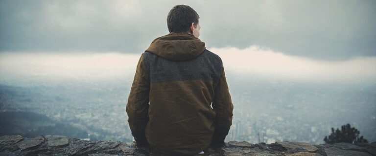 A sitting man is shown from behind, overlooking a city