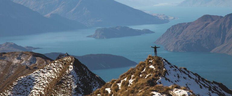 A woman stands atop a hill, arms open wide