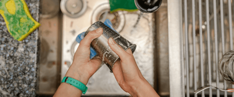 person washing a metal cup in a kitchen sink