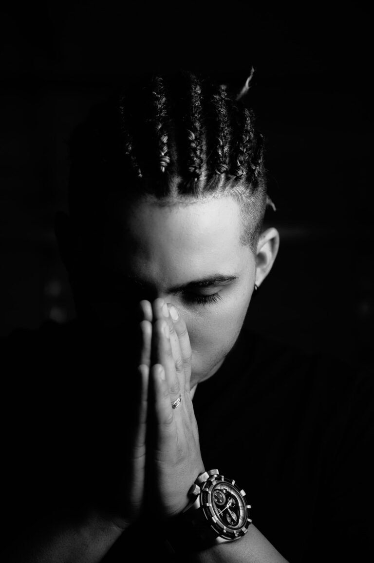 A man with braids closes his hands to pray