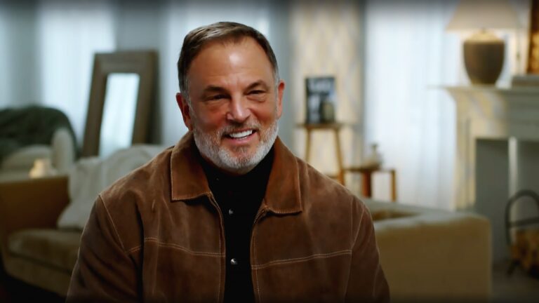 A bearded man smiles and talks