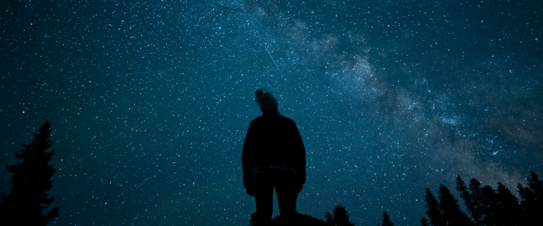 Silhouette of a person outside at night staring at the sky